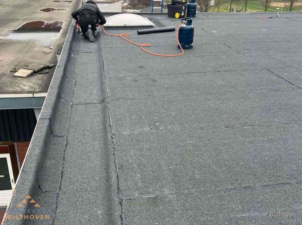 Dakdekker repareert bitumen dakbedekking op groot plat dak in Bilthoven